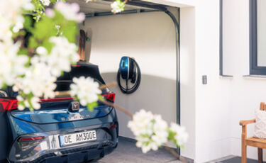 Elektroauto wird in einer Garage mit einer MENNEKES Wallbox aufgeladen, blühende Pflanzen sind im Vordergrund.